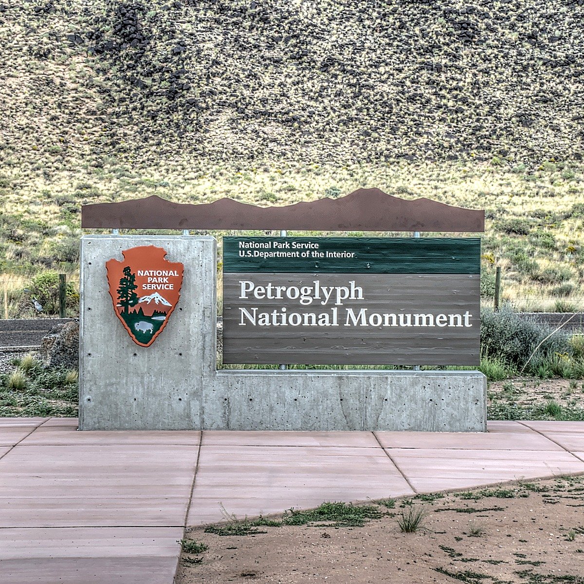 Outdoor monument sign on a stone and steel base structure National Park Service monument sign on a stone-and-steel base structure set in an exposed outdoor landscape