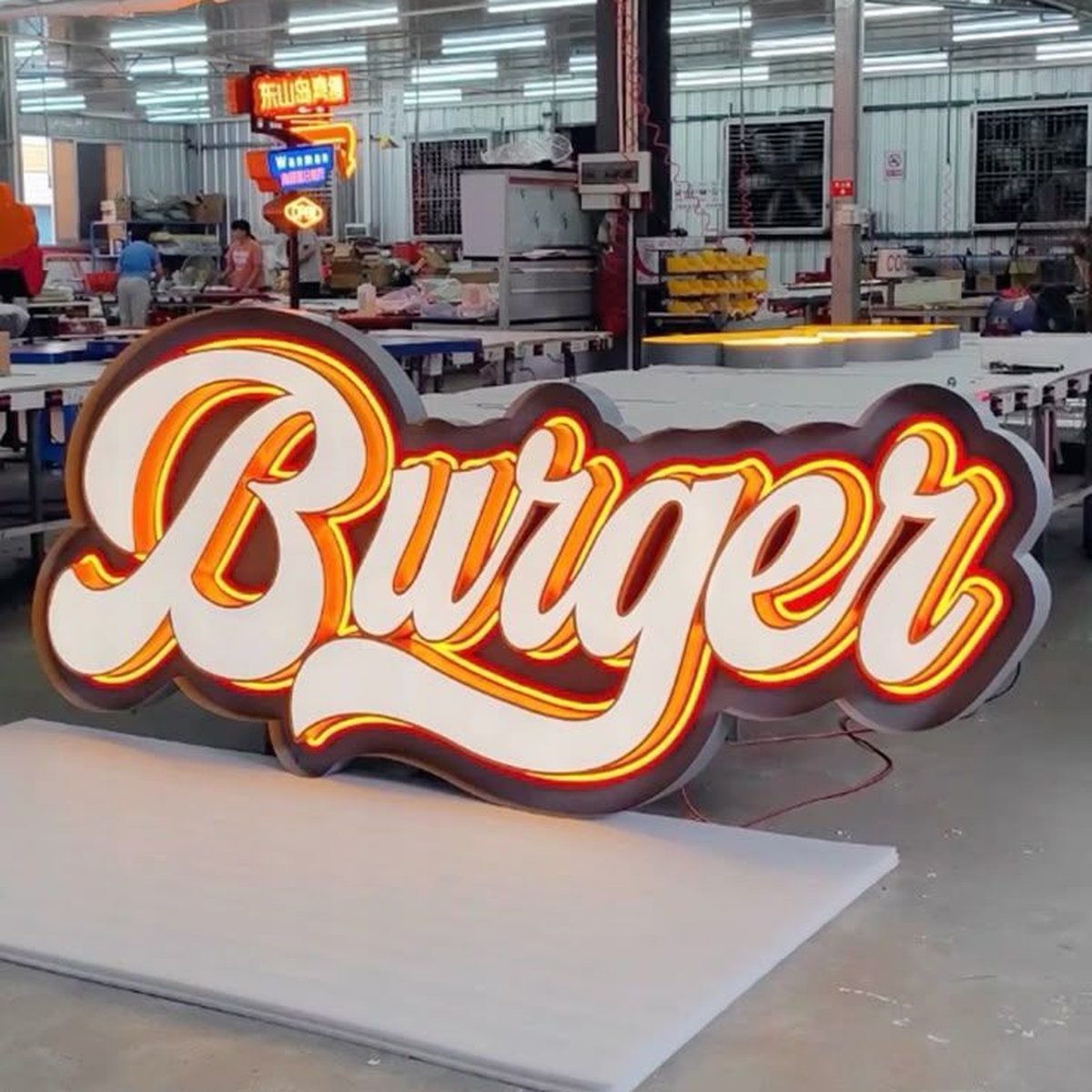 Burger illuminated sign with orange halo lighting powered on in a factory.
