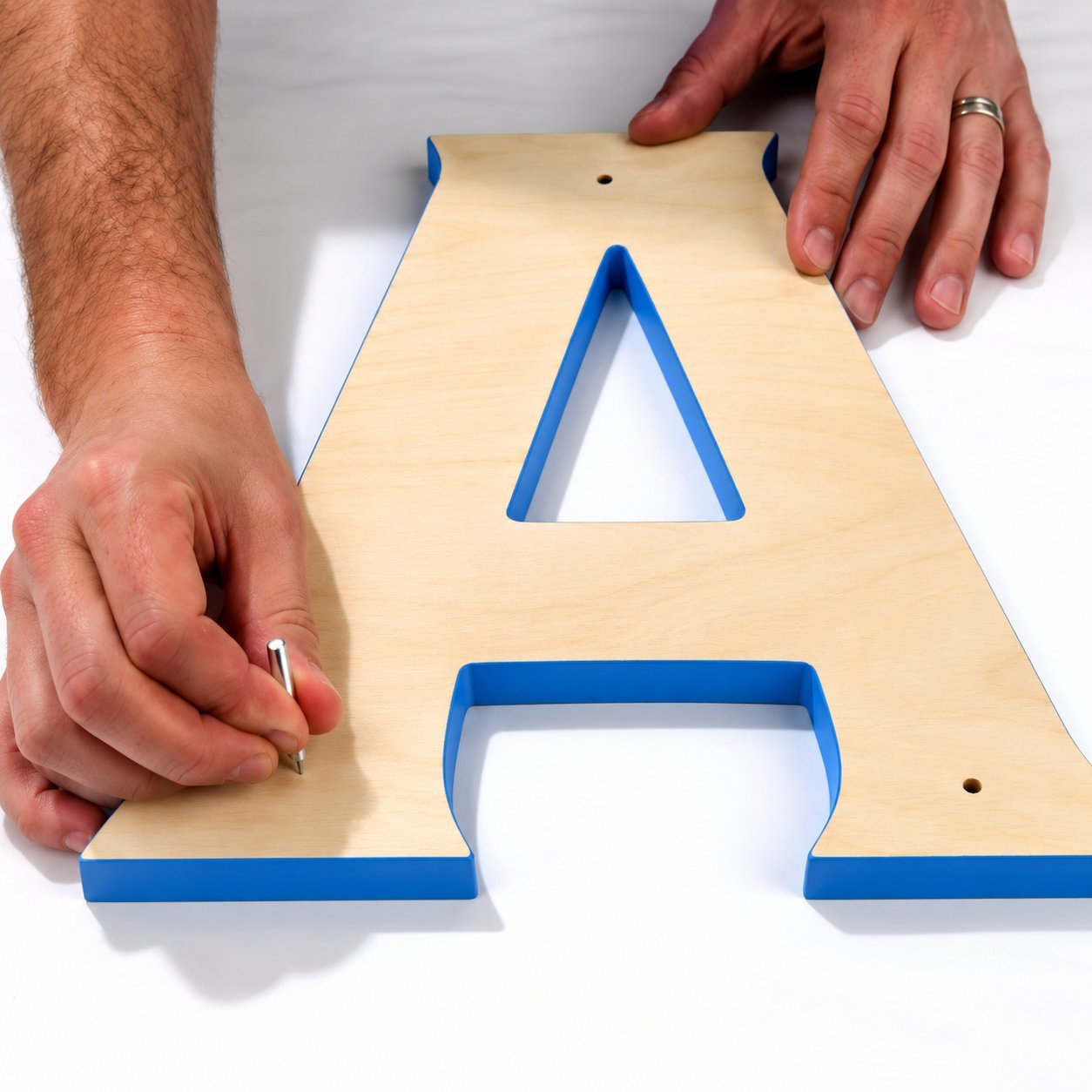 Hands marking a wooden letter A on a work surface — DIY sign design and fabrication step.
