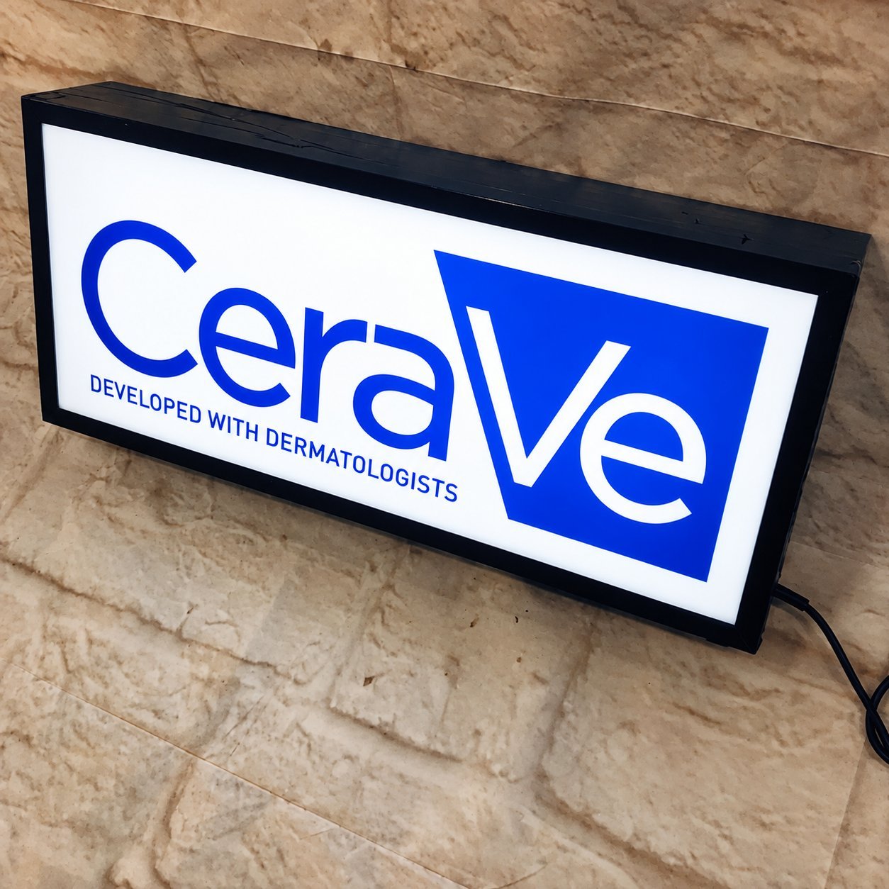 CeraVe lightbox sign with blue logo on a stone wall, an example of finished factory-produced illuminated signage.