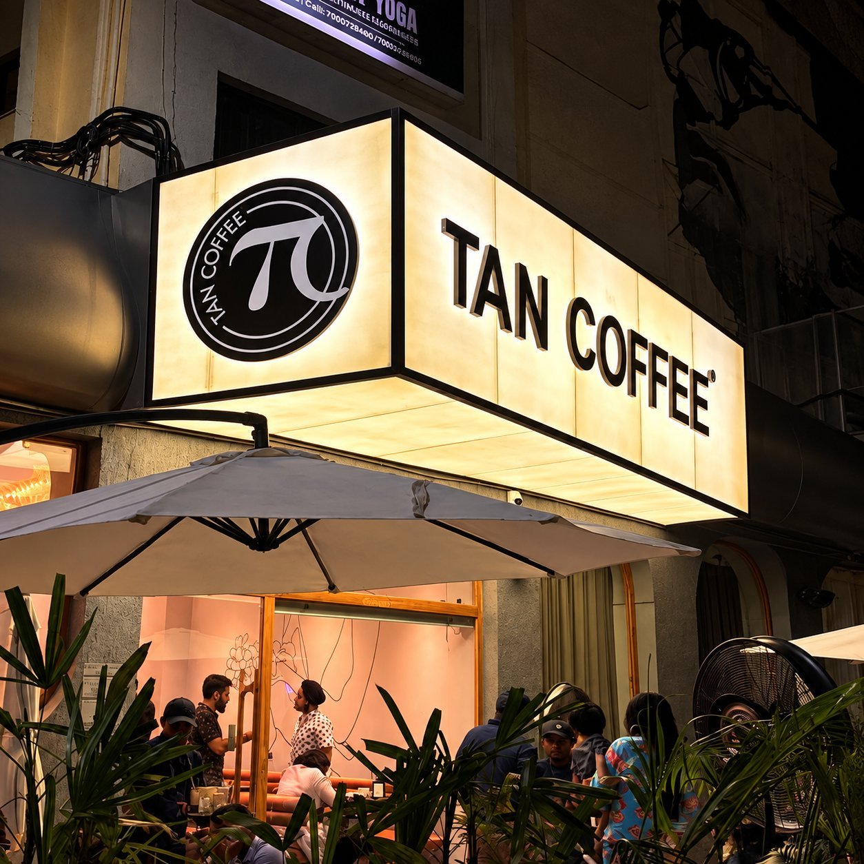 Tan Coffee illuminated signage over a busy evening storefront with warm white LED face.