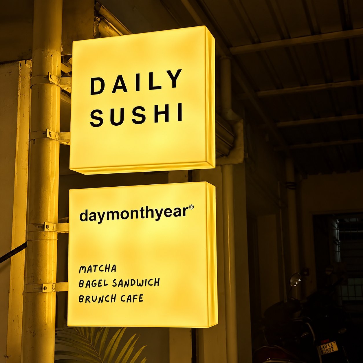 Daily Sushi yellow lightbox sign stack on a steel pole outside a brunch cafe.