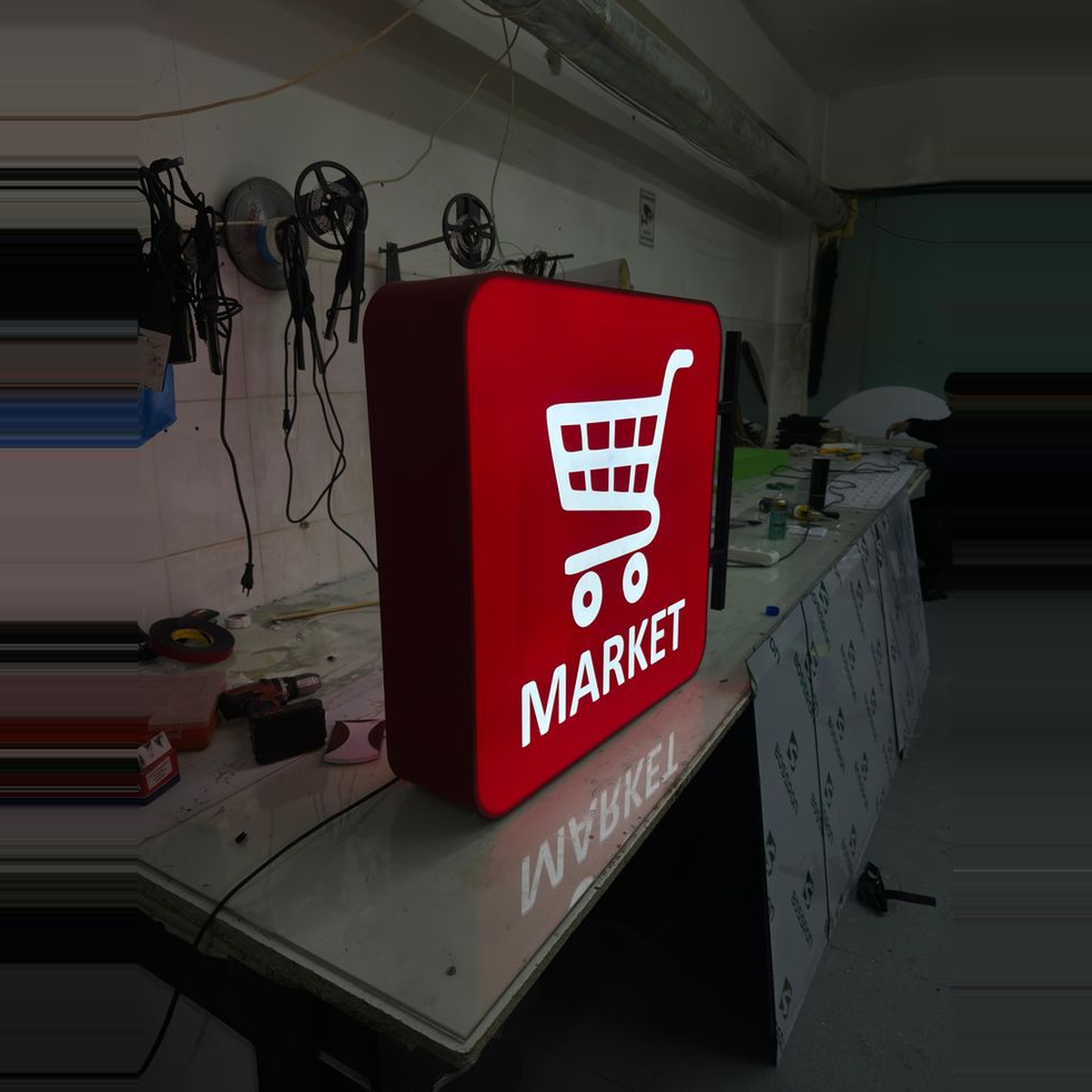 Illuminated MARKET sign on a workshop table surrounded by wiring and soldering tools.