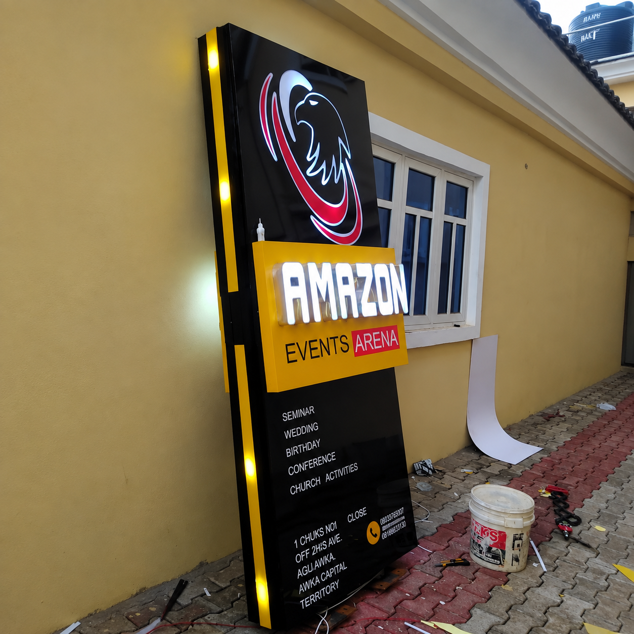 Finished black and yellow illuminated event-venue sign standing beside a building.