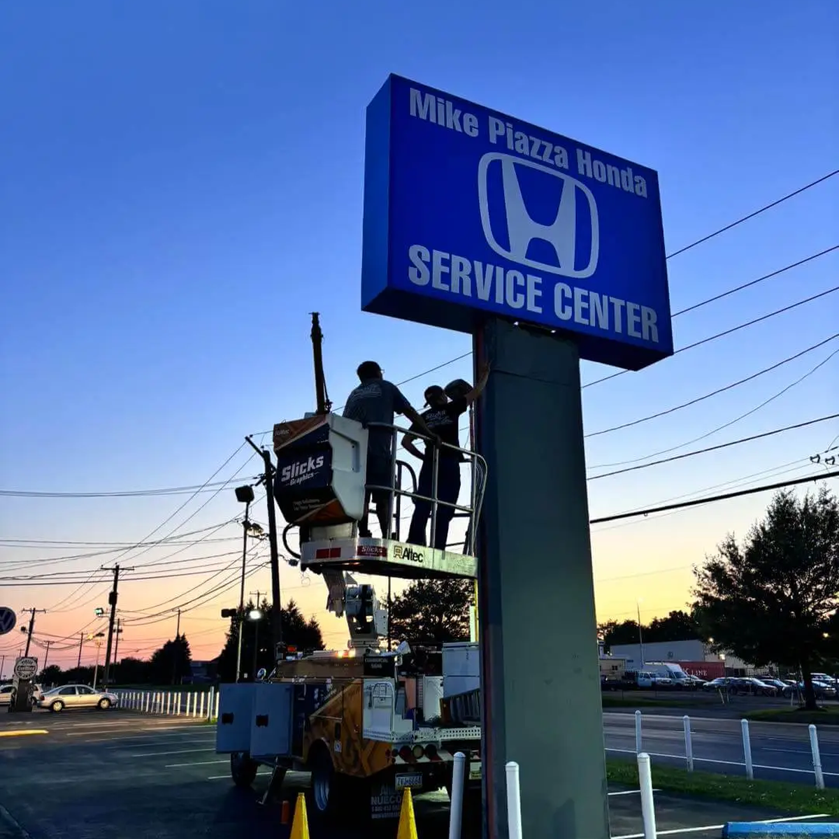 Installers in an elevated bucket working beside a blue service-center pylon sign.