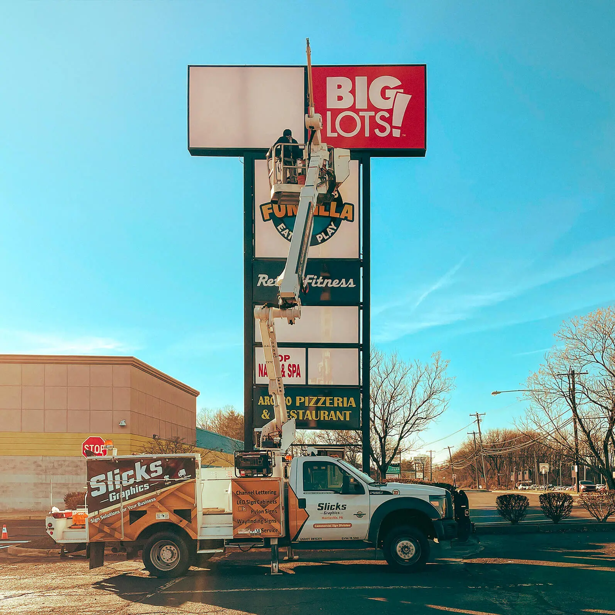 Bucket truck beside a tall multi-tenant pylon sign during on-site sign work.