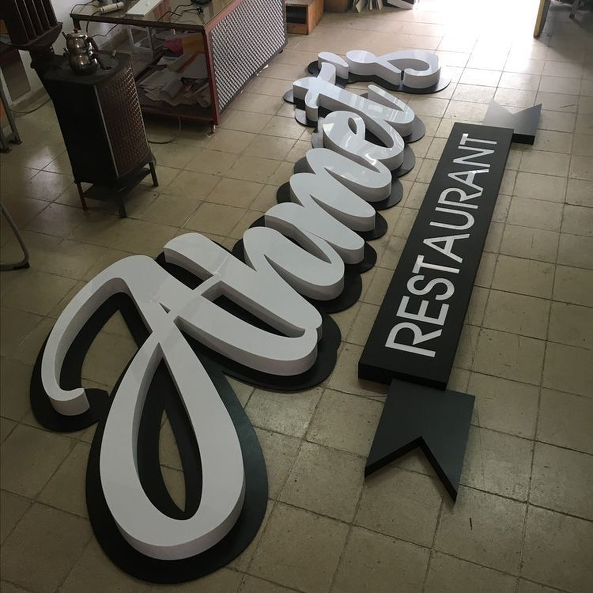 Large ORANZ RESTAURANT channel letters and black plaque laid out on a factory floor.