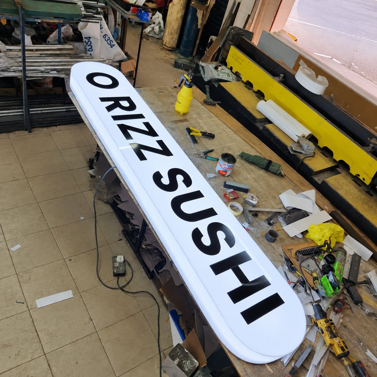 Long white ORANZ SUSHI channel letter assembly resting on a factory workbench.