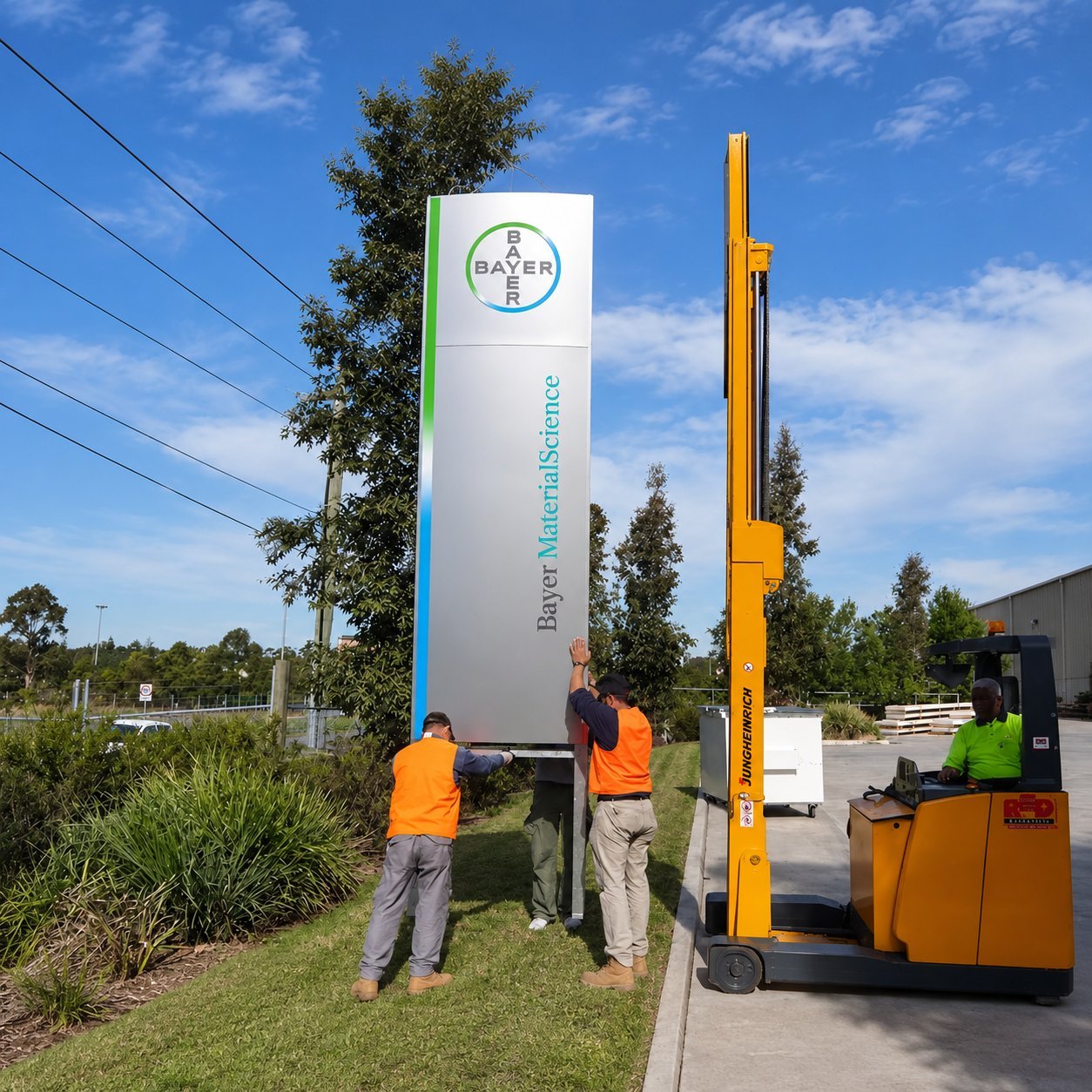 Pylon Installation Crew Installation crew aligning a tall Bayer MaterialScience pylon sign with a forklift on site.