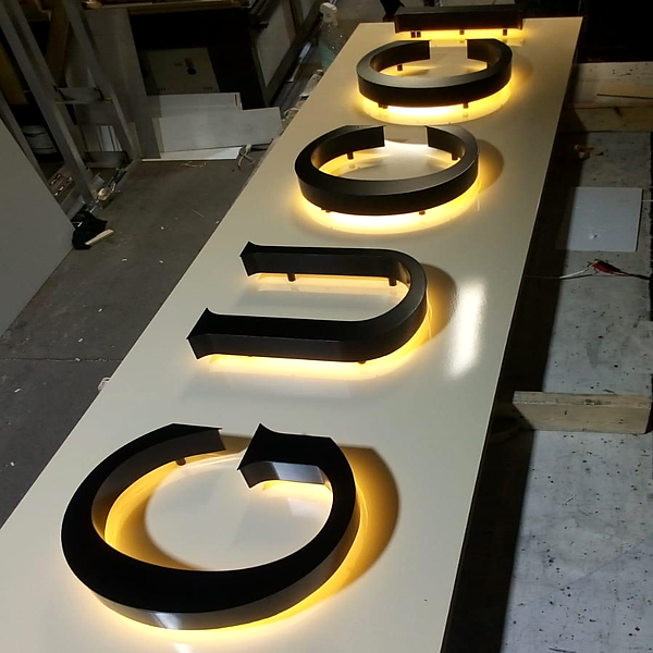 Dimensional storefront letter with halo backlight glow on a workshop table