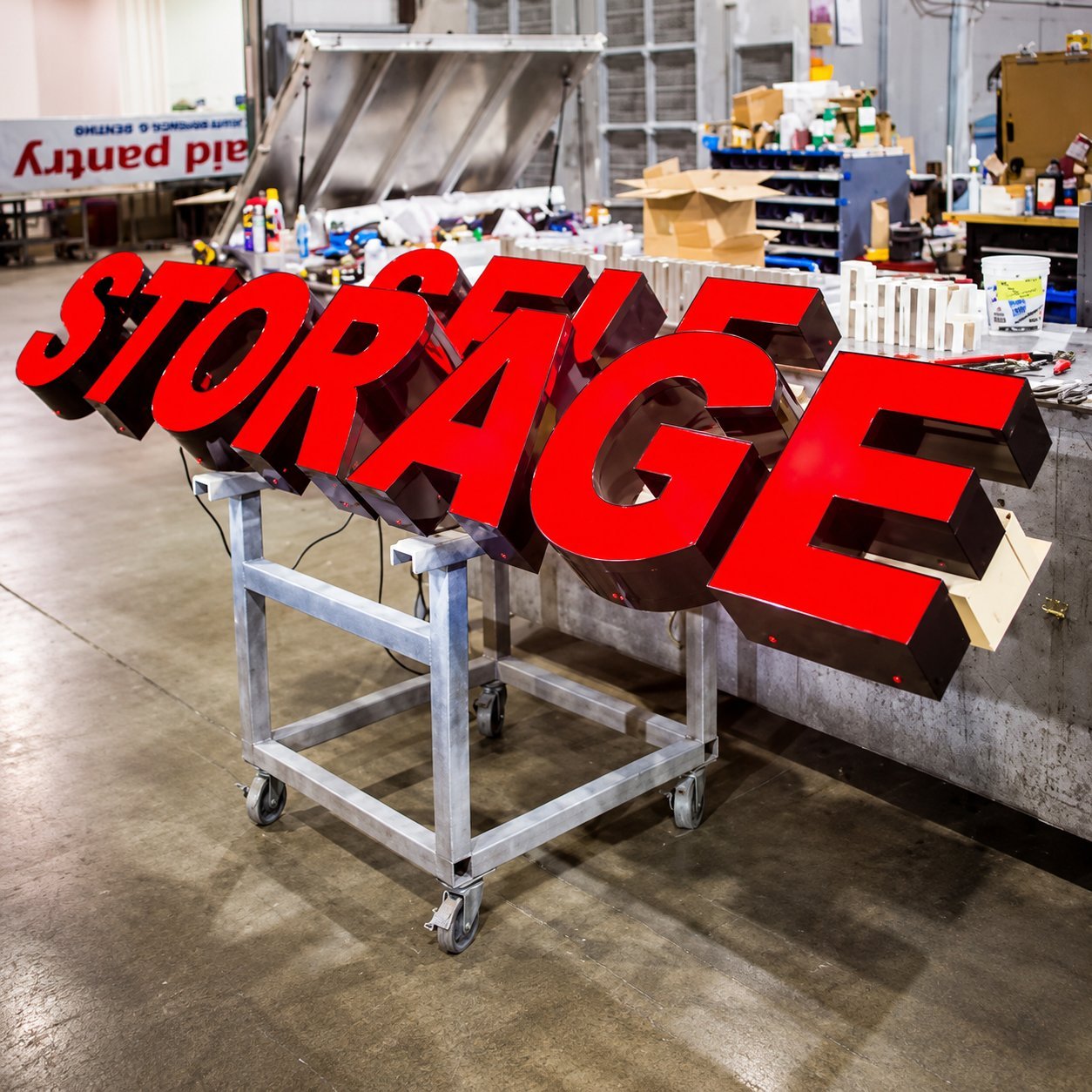 Red three-dimensional illuminated STORAGE channel letters on a rolling work stand in a Hicen workshop, before final assembly.