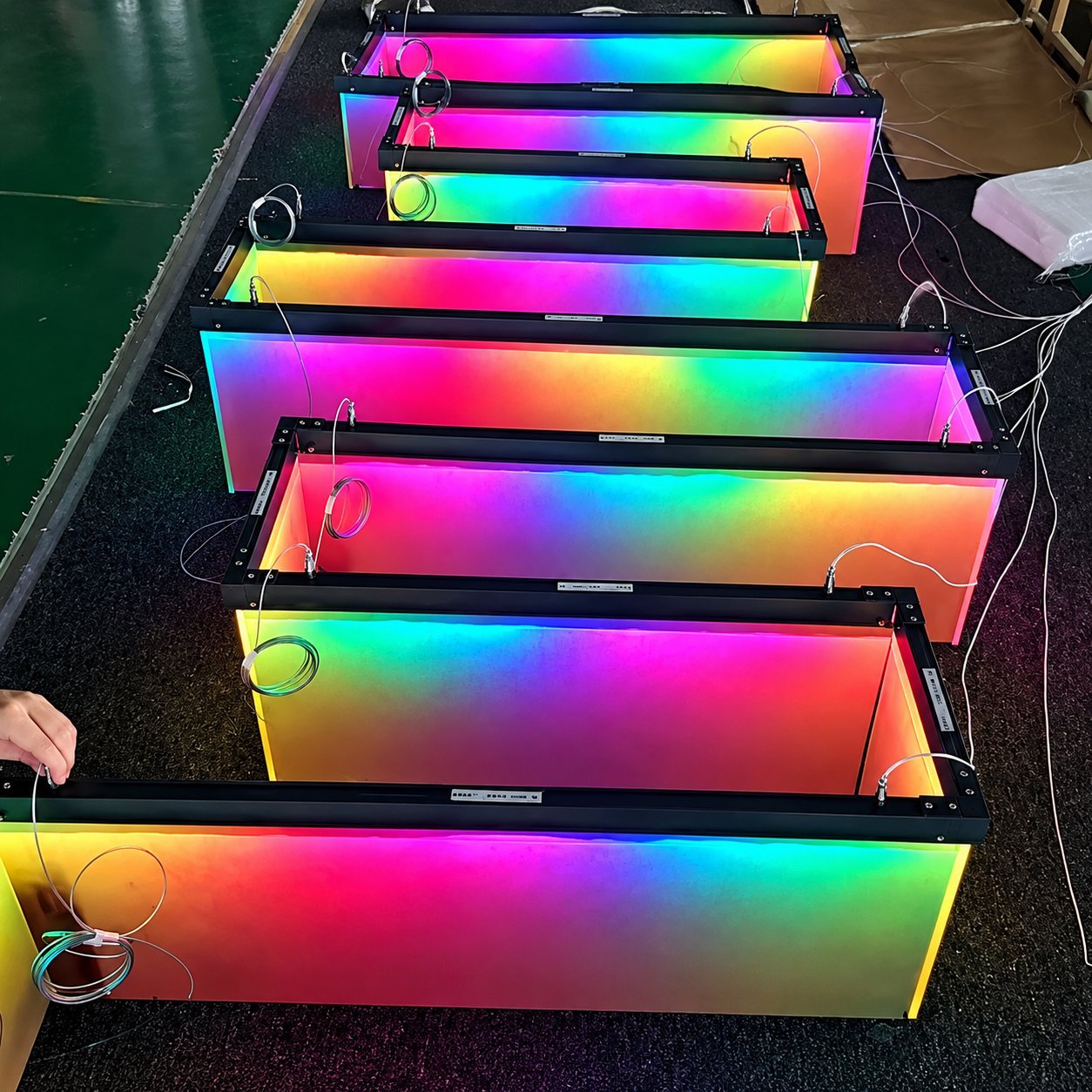 Workshop row of LED light boxes glowing in a smooth RGB rainbow gradient during pre-shipment inspection.